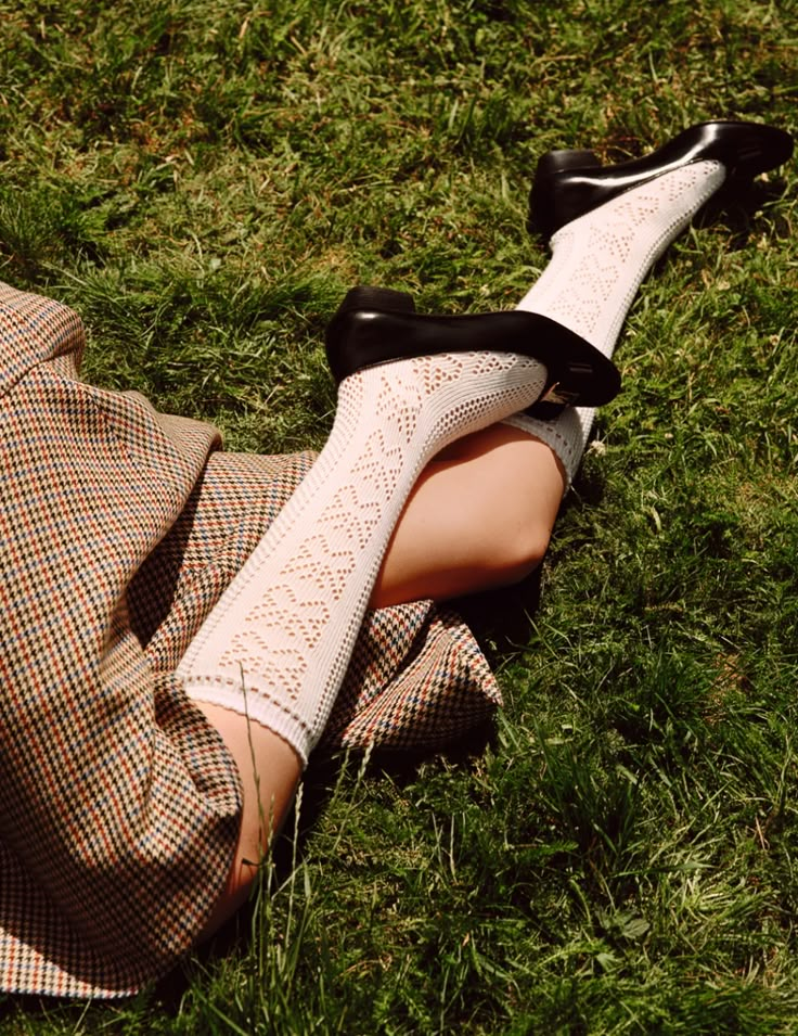 a woman laying in the grass with her legs crossed wearing white socks and high heels