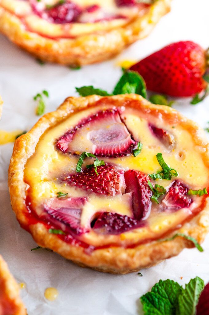 strawberry tarts with cheese and fresh strawberries on white paper next to lemon wedges