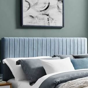 a bed with blue headboard and white pillows in a green room next to a painting on the wall