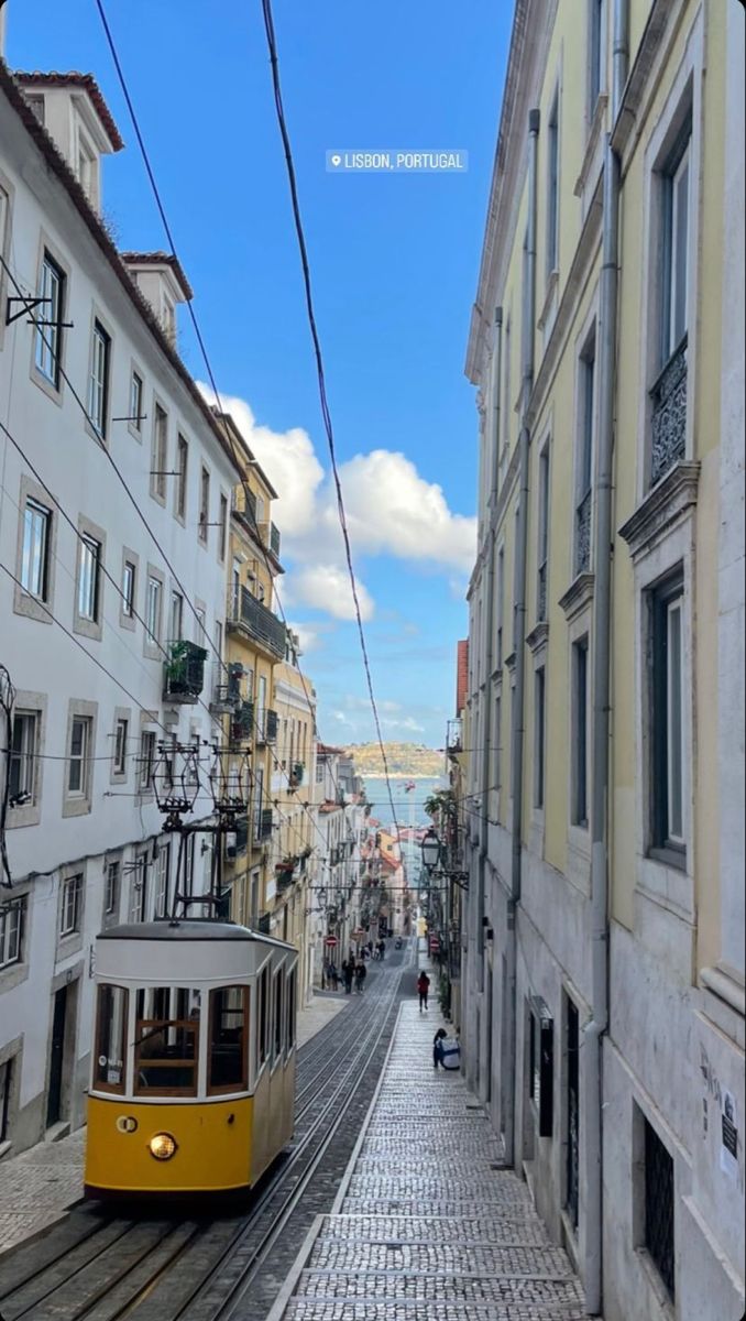 a yellow trolley is going down the street in front of some white buildings and people