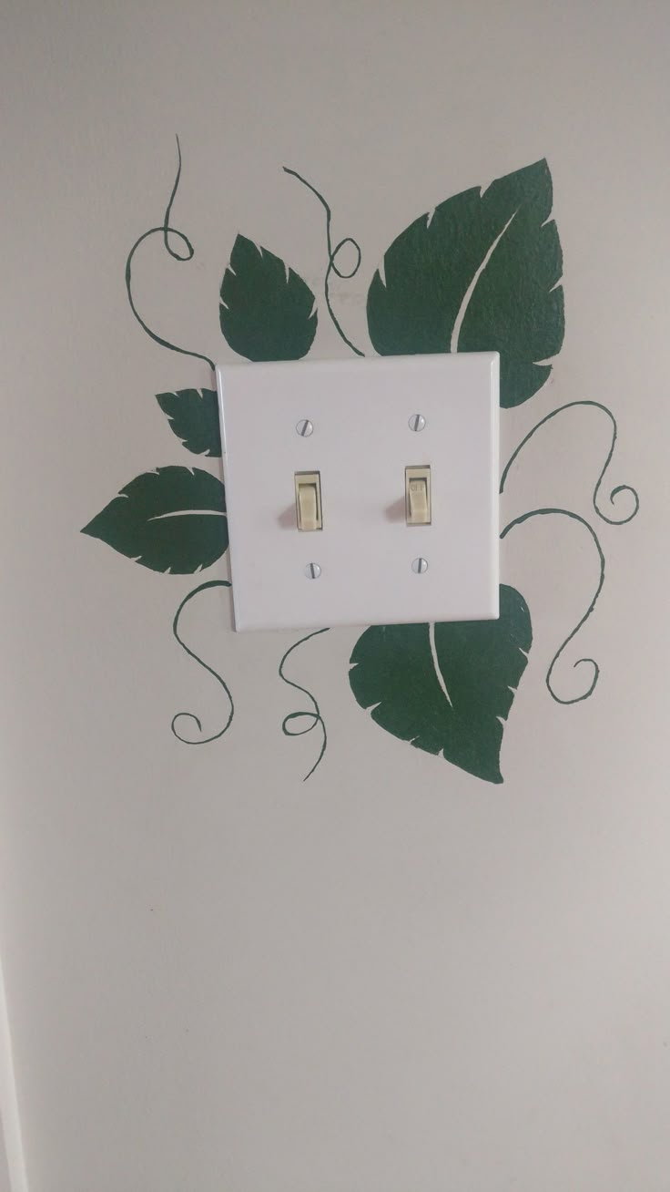 a white light switch sitting on top of a wall next to a green leaf design