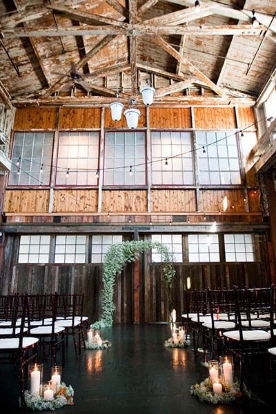 the inside of an old barn with candles and greenery on the aisle, surrounded by wood paneling