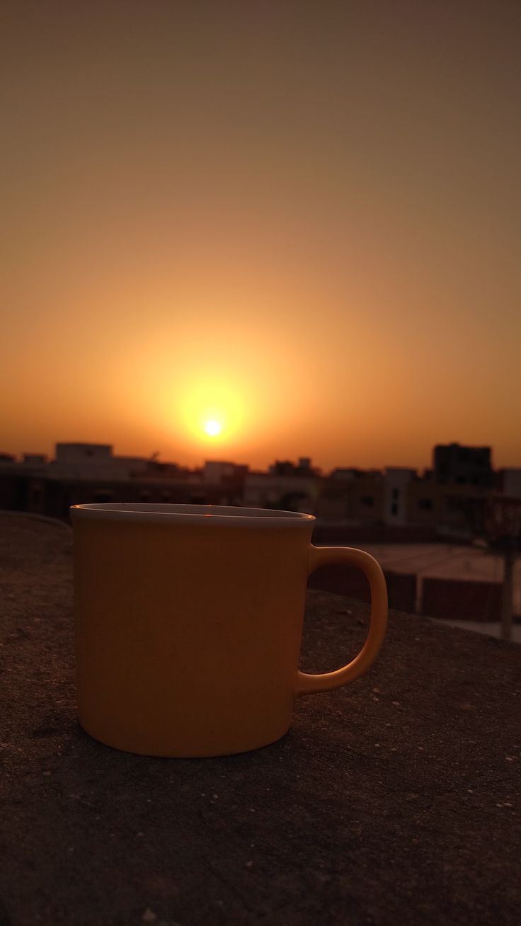 a yellow coffee cup sitting on top of a wooden table in front of the sun