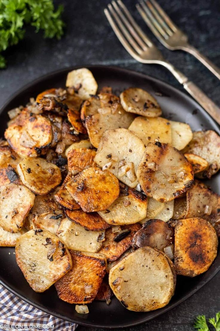 a black plate topped with cooked potatoes next to a fork and parsley on the side