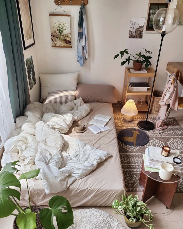 an unmade bed sitting in a bedroom next to a table with plants on it