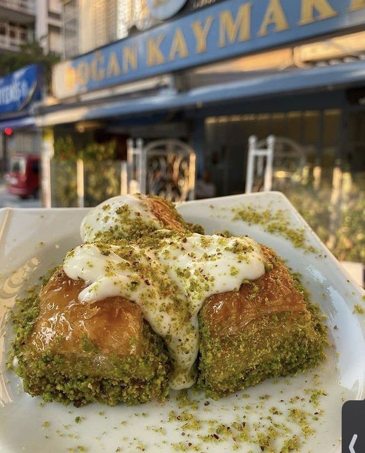 a white plate topped with two pieces of food covered in sauce and pesto next to a building