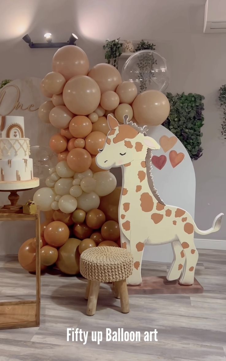 a giraffe is standing next to balloons and a table with a cake on it