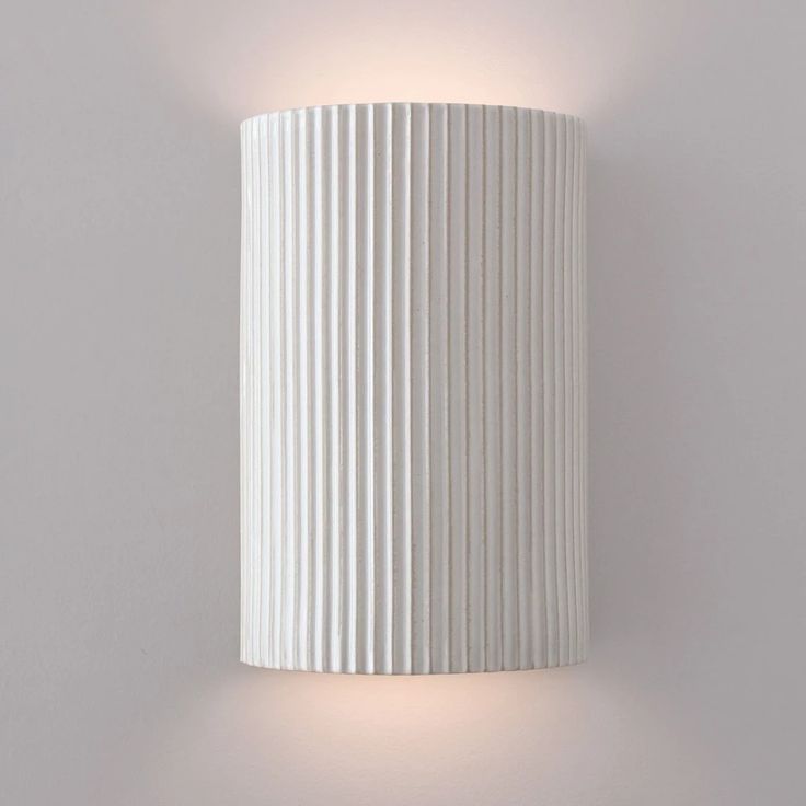 a white wall mounted light with pleated paper covering it's face and arm