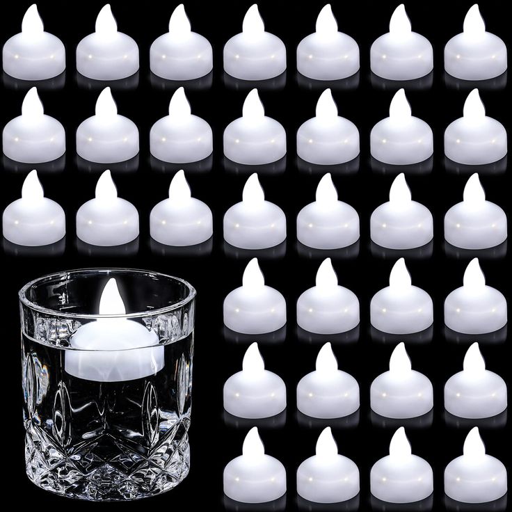 a glass filled with lots of white candles next to a candle holder on a black background