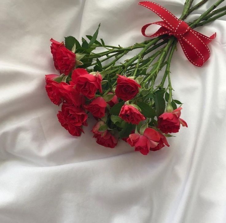 a bunch of red roses tied together with a bow on a white cloth covered bed