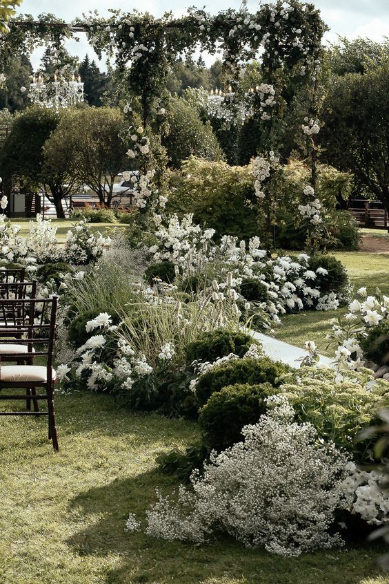 chairs are set up in the middle of a garden with white flowers and greenery