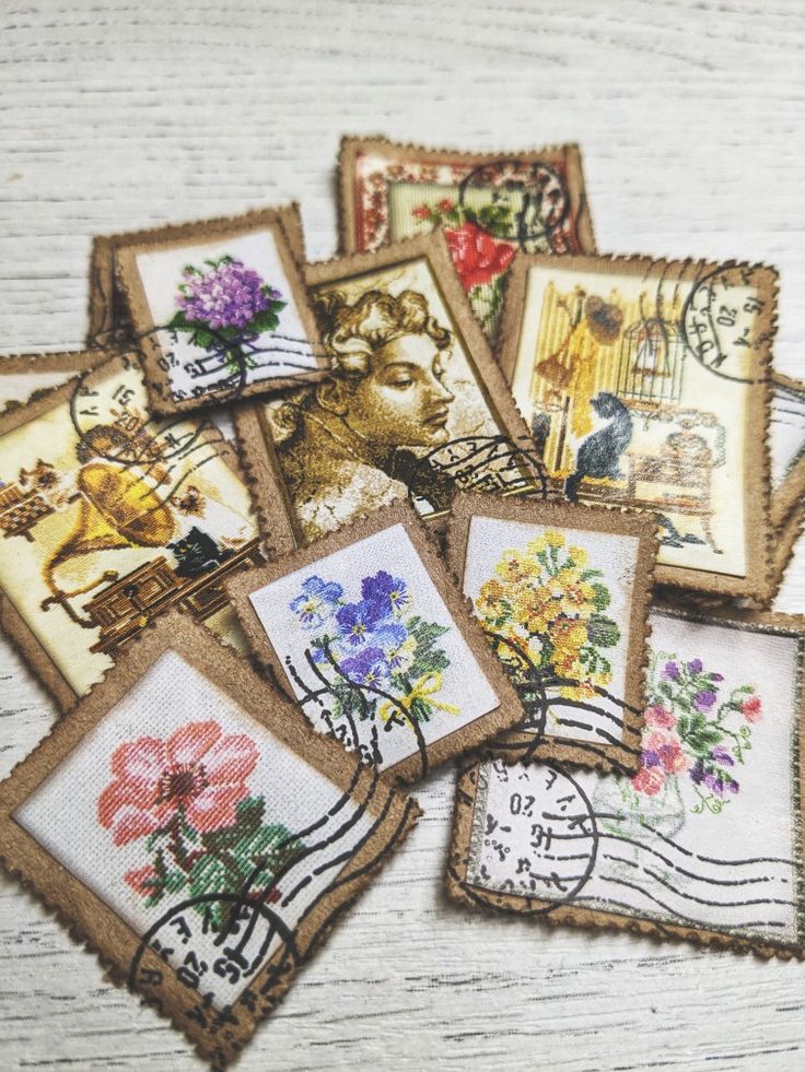 small embroidered postcards with pictures of flowers and birds are on a white wooden surface