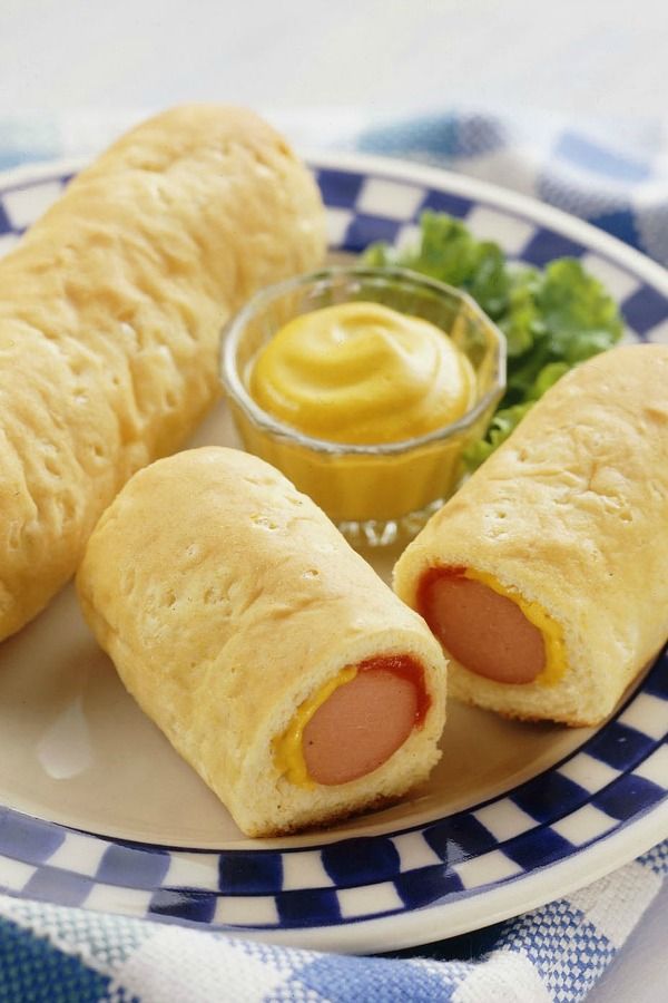 two sausage rolls on a plate with mustard and lettuce next to it, ready to be eaten