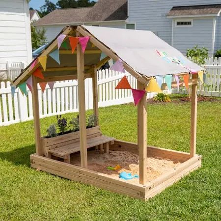 a small wooden play house with flags on the roof and sand in the bottom half