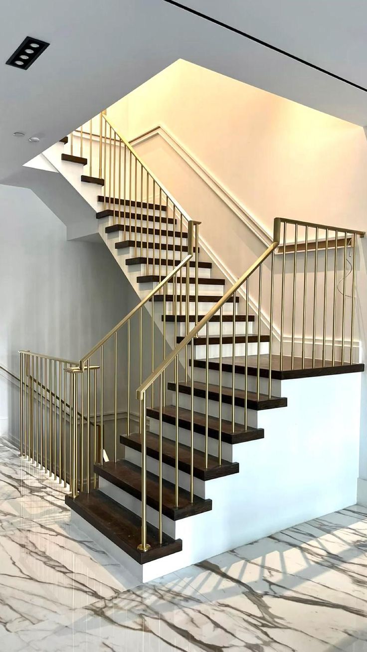 a staircase in an empty room with marble flooring and white walls, along with gold handrails