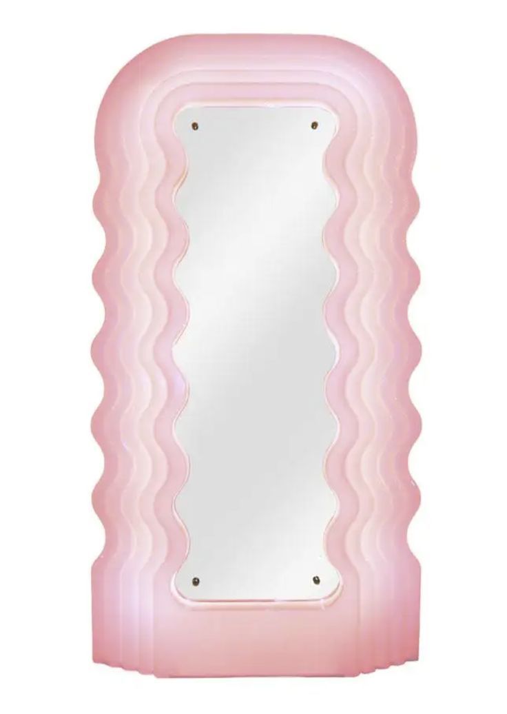 a pink mirror sitting on top of a white table next to a wall mounted light