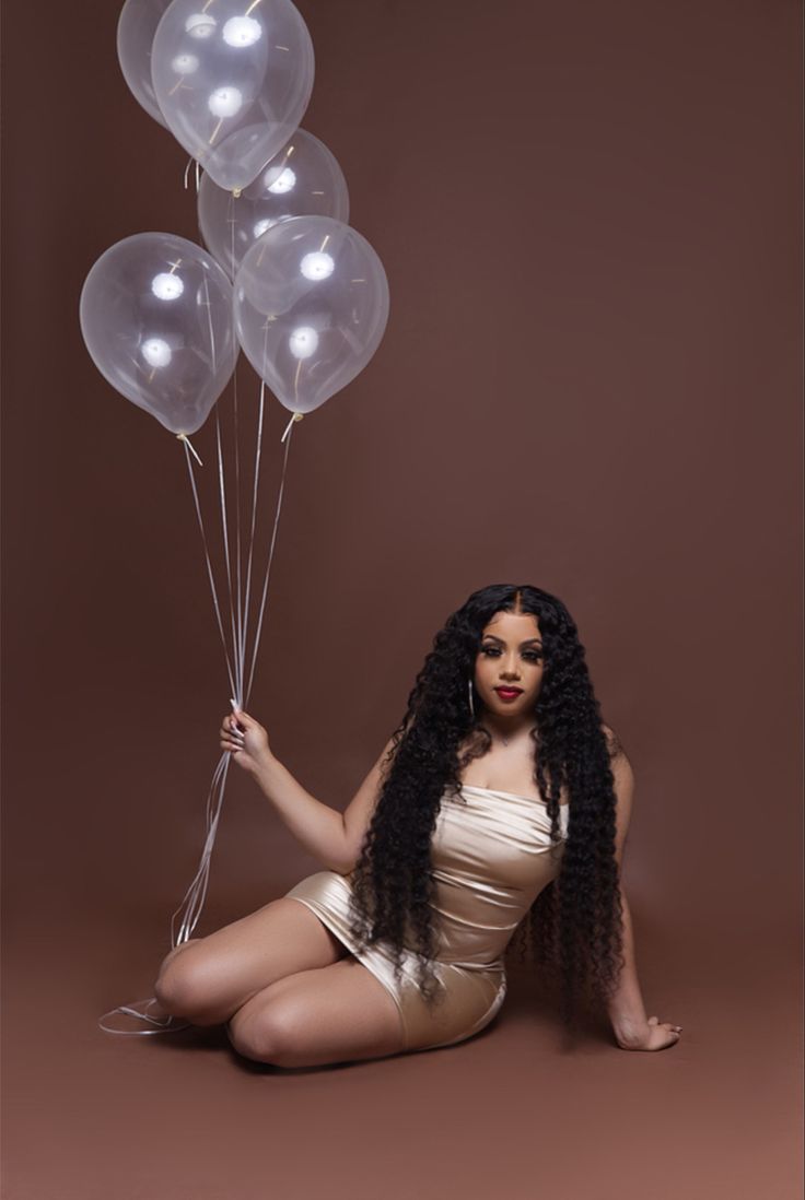 a woman sitting on the ground with balloons in front of her, wearing a gold bodysuit