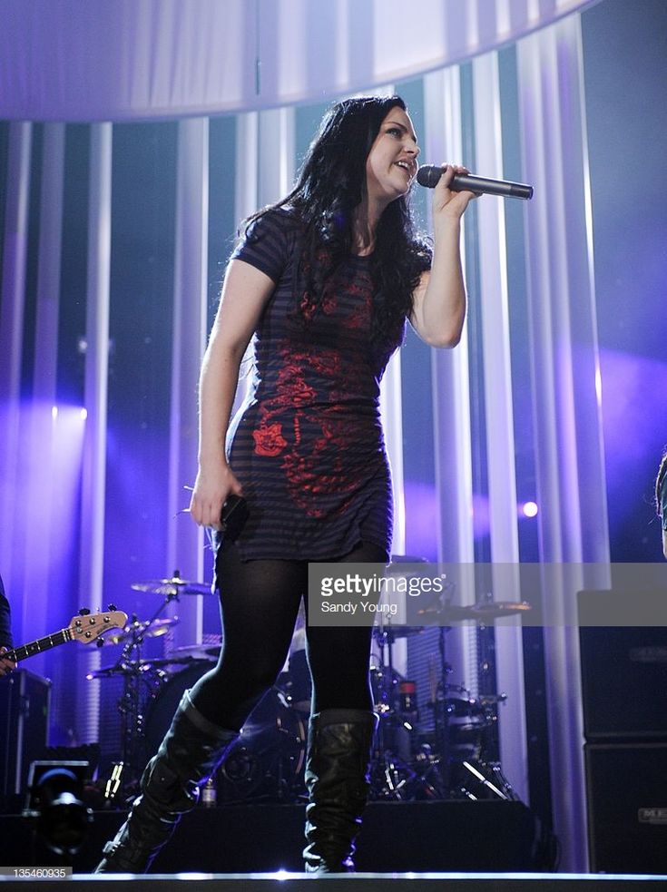 a woman singing into a microphone while standing in front of a stage with other instruments