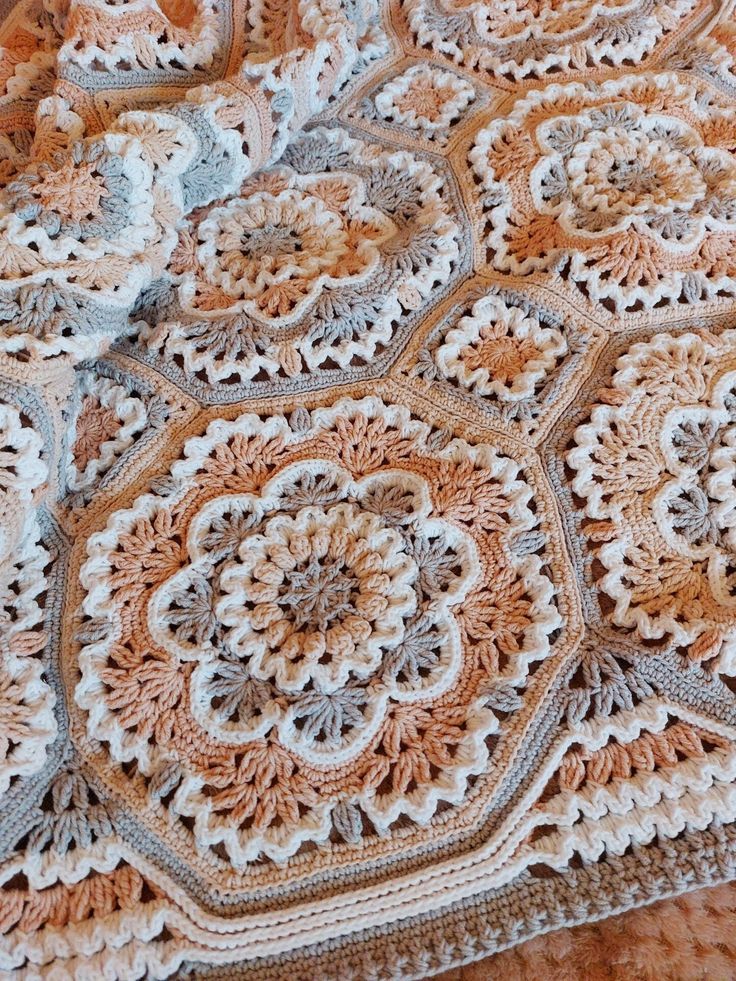 a crocheted blanket is laying on top of a wooden table with an orange and white doily