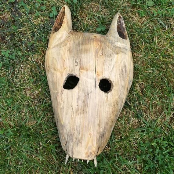 a wooden mask laying in the grass with two holes cut into it's face