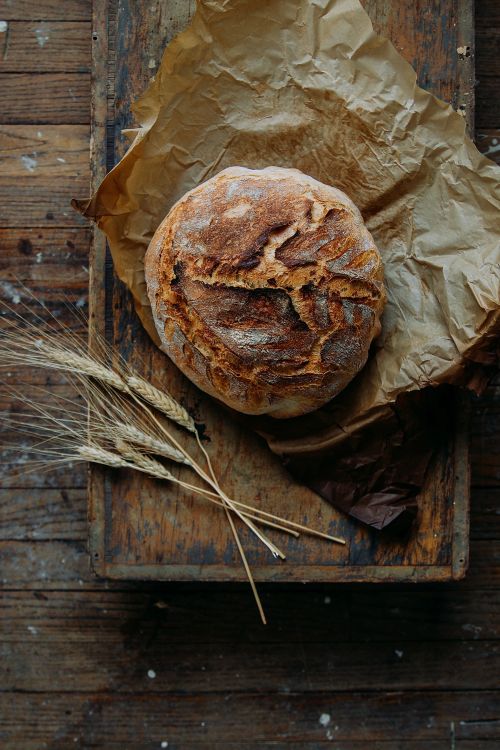 a loaf of bread sitting on top of a wooden cutting board next to some wheat