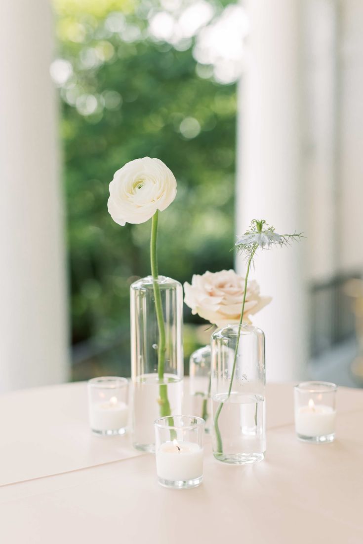 three vases filled with flowers on top of a table next to candles and water