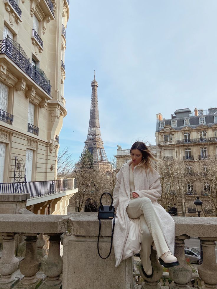 a woman sitting on a ledge in front of the eiffel tower