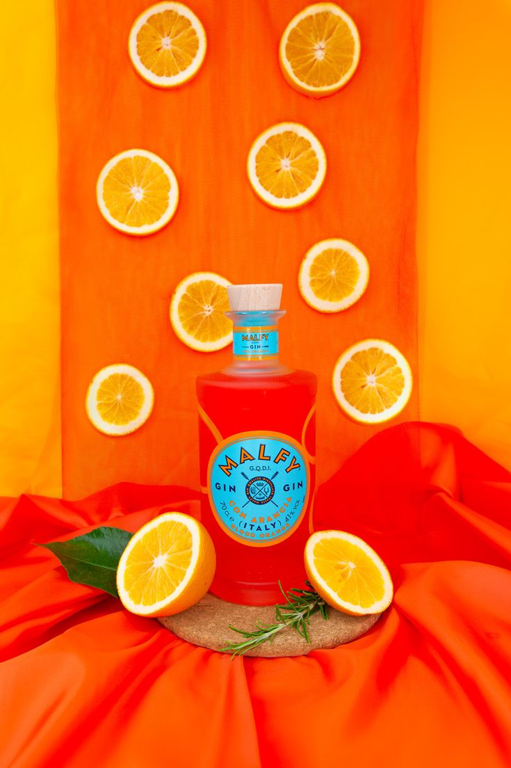 a bottle of orange juice surrounded by slices of oranges on a red cloth with an orange background