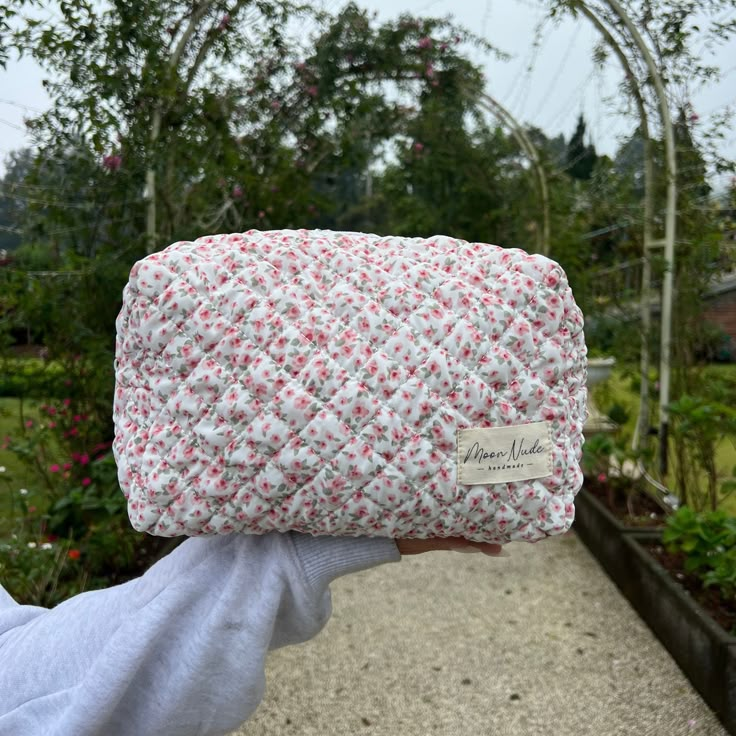 a person holding up a pink and white bag in front of some plants on the sidewalk