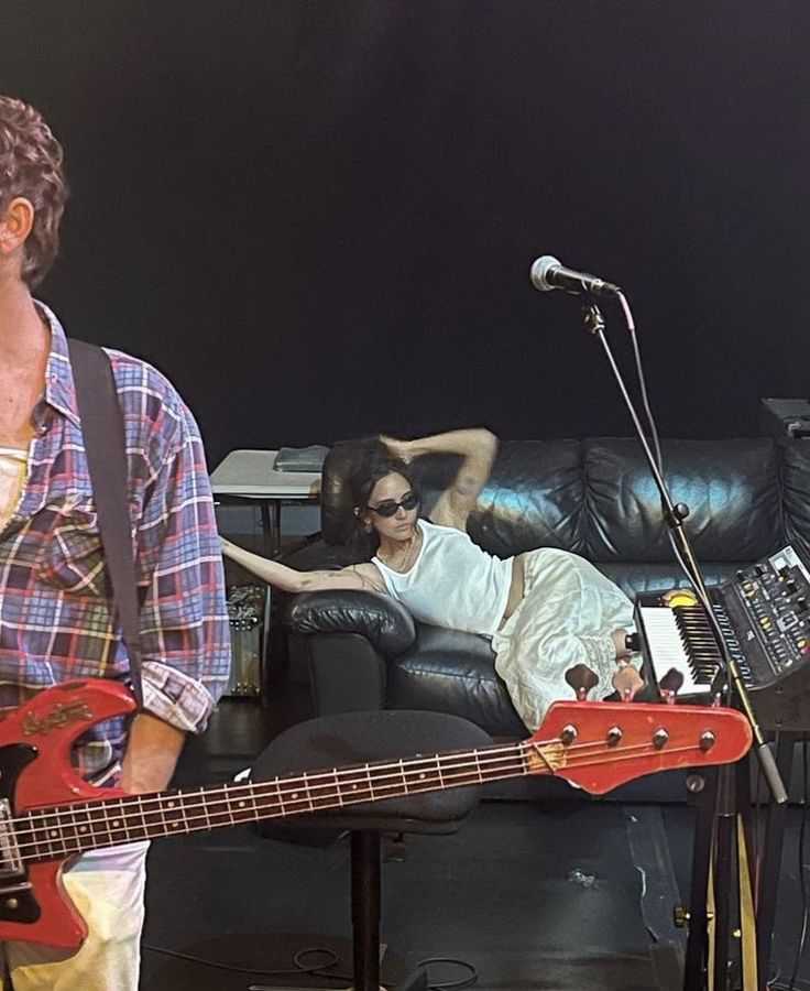 a man is sitting on a couch while holding a guitar and playing the bass in front of him