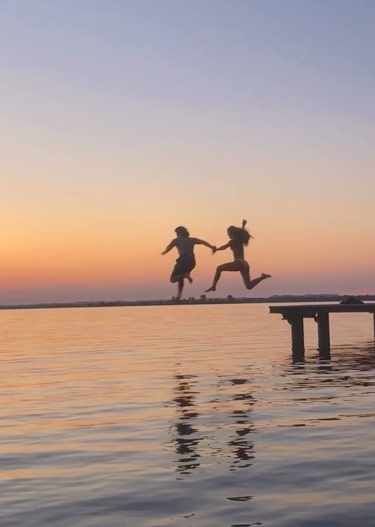 two children jumping into the water at sunset