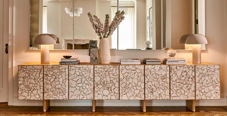 a white and gold sideboard with two lamps on it in front of a mirror