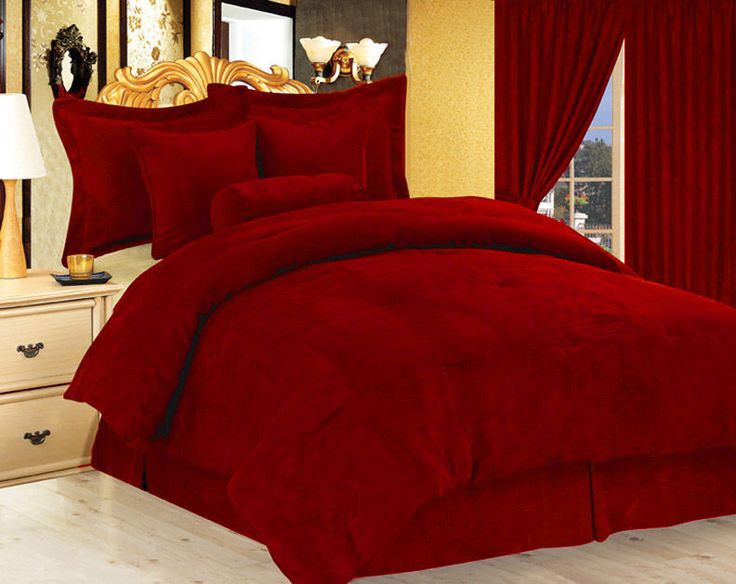 a bed with red comforter and pillows in a room next to a window,