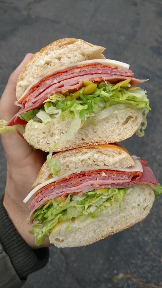 a person holding two halves of a sandwich in their left hand, with lettuce and meat on it