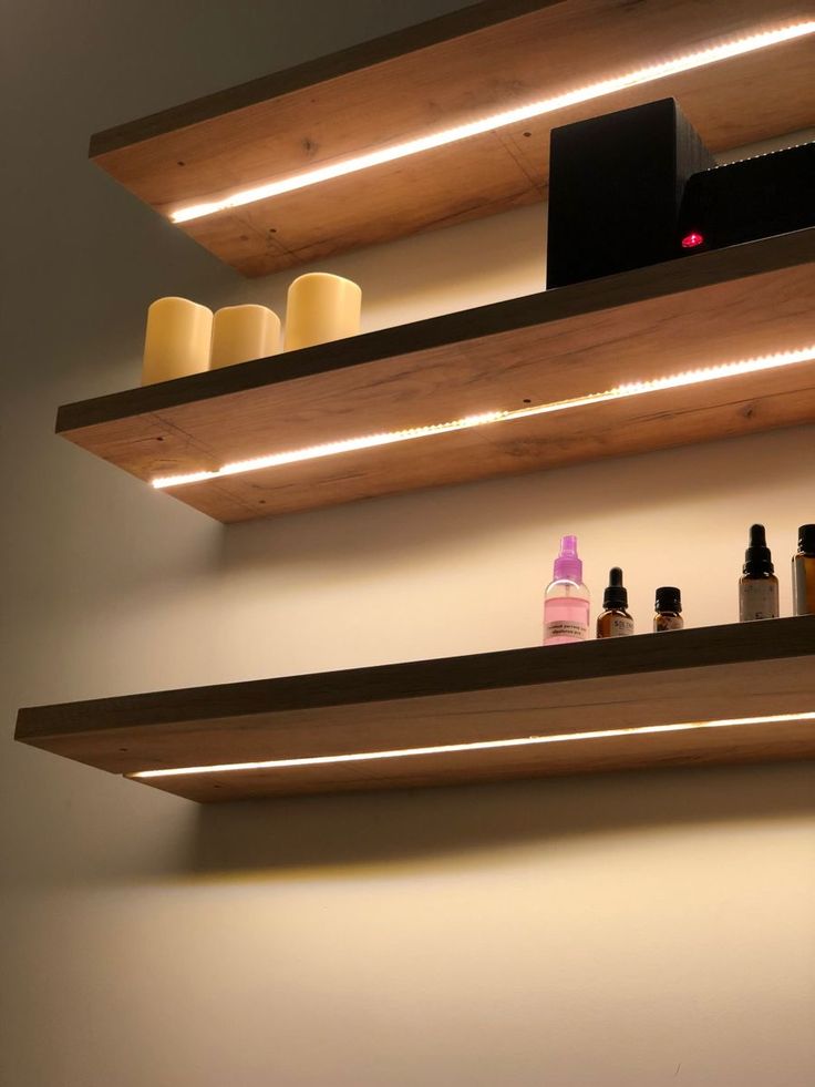 shelves with bottles and candles on them in a bathroom area that is lit up at night