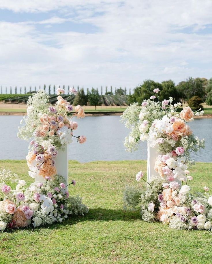 two tall vases with flowers are sitting in the grass near some water and trees