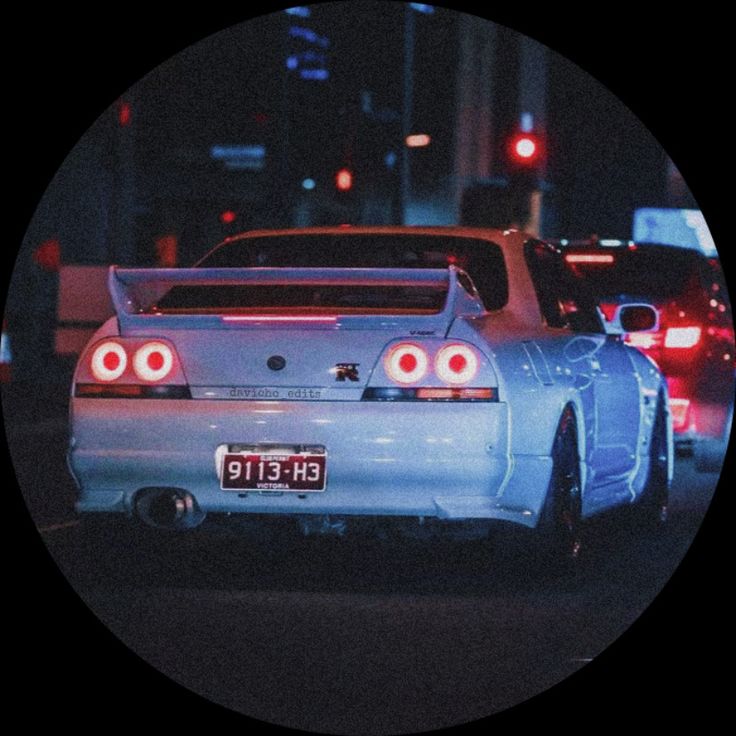 the back end of a white car on a city street at night