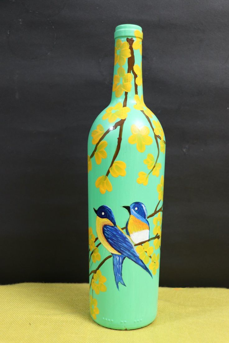 a blue and yellow vase with two birds on it sitting on a table next to a black wall