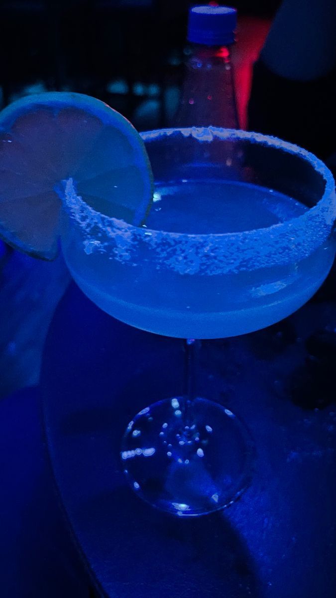 a blue lit up cocktail with a lime slice on the rim in front of it