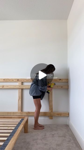 a woman standing in front of a wooden bunk bed holding a screwdriver and looking at the wall