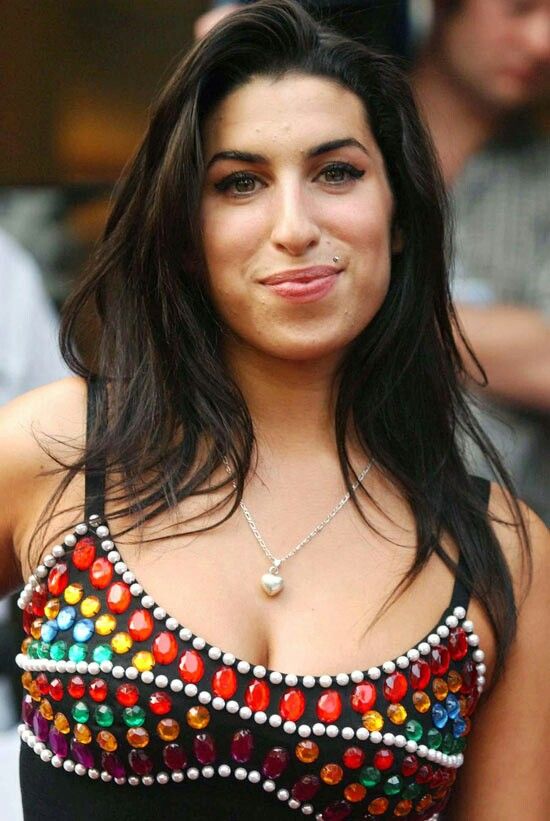 a woman with long hair wearing a black top and colorful beads on her chest is smiling at the camera