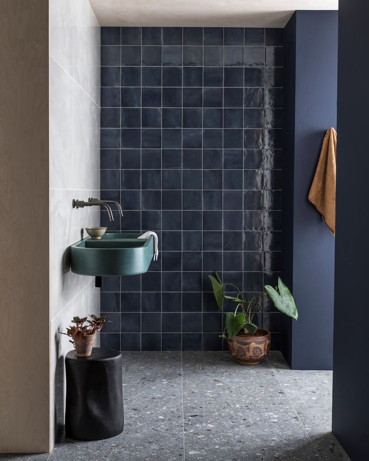 a blue tiled bathroom with a green sink and black tile on the wall, along with potted plants