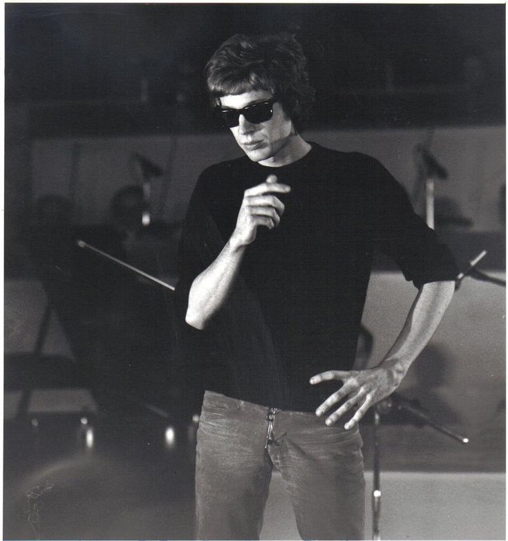 a man standing in front of a microphone with his hand on his chin and wearing sunglasses