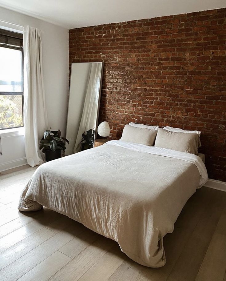 a bedroom with brick wall and white bedding, windows, and wooden flooring