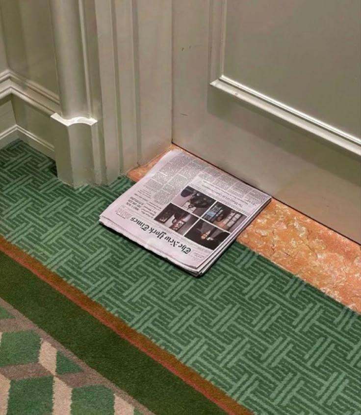 a newspaper laying on the ground in front of a door with green and brown carpet