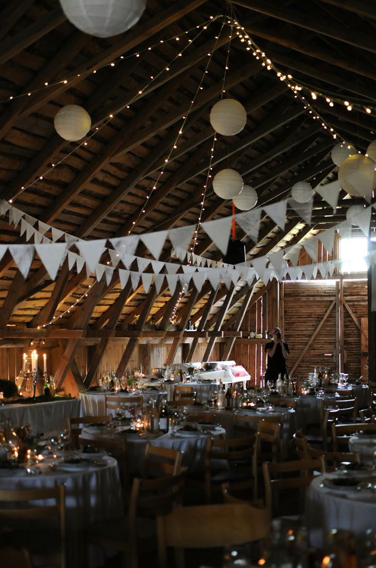 tables and chairs are set up in the barn for an event with paper lanterns hanging from the ceiling