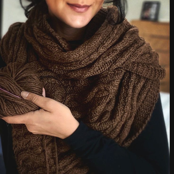 a woman wearing a brown scarf and holding a ball of yarn