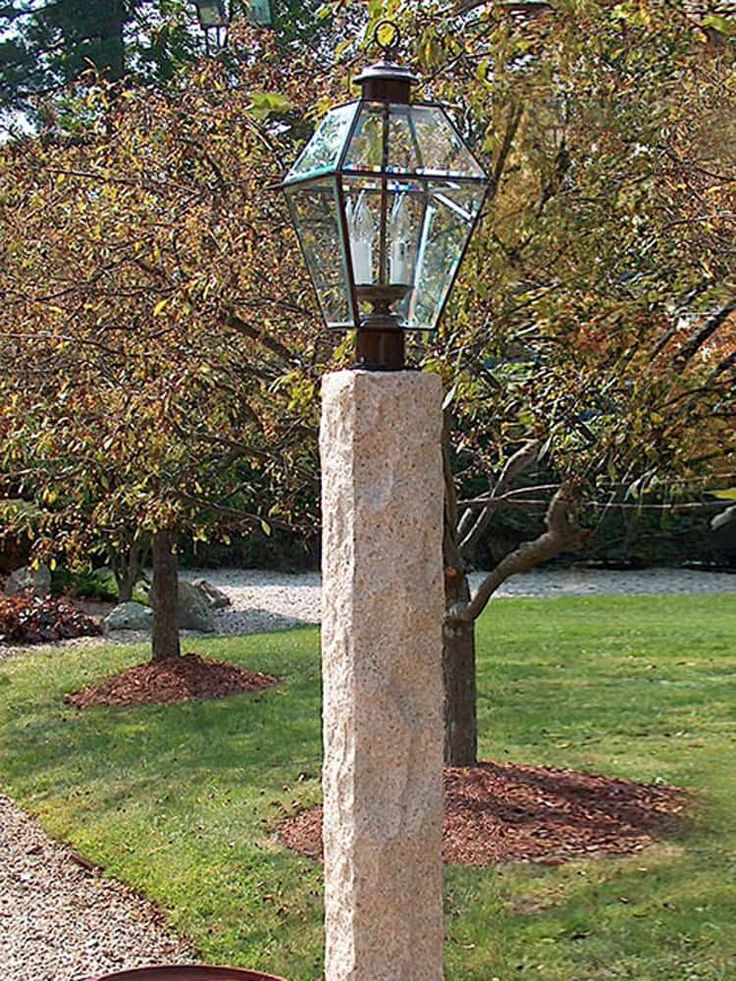 a stone lamp post in the middle of a grassy area with trees and bushes behind it