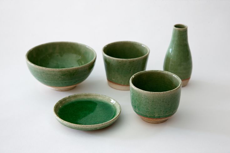 four green bowls and two vases on a white surface