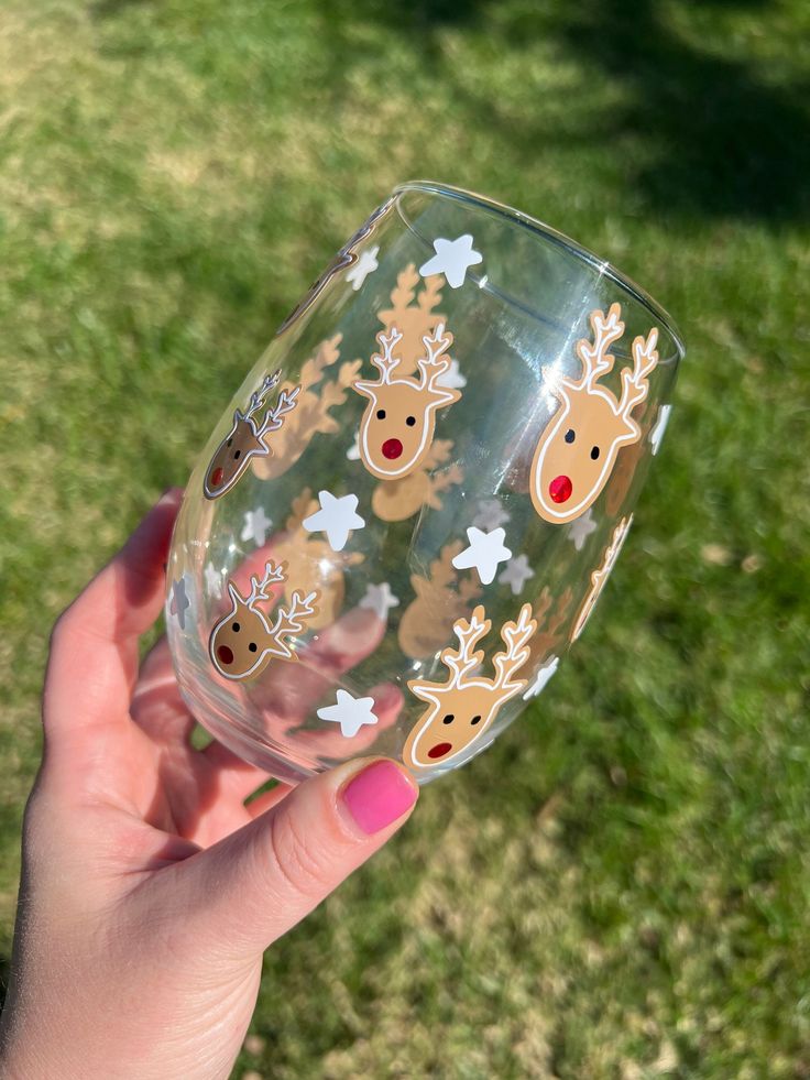 a hand holding up a wine glass with reindeer decals and snowflakes on it